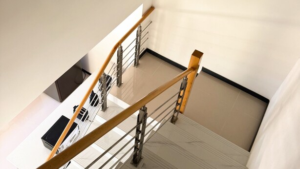 Un escalier avec une main courante en bois, des rampes en métal et un sol carrelé.