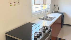 Une cuisine avec des meubles de rangement en bois, une cuisinière, un évier et une fenêtre avec des rideaux.
