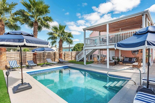 Ein Schwimmbad mit Liegestühlen und Sonnenschirmen, eine überdachte Terrasse und ein Holzzaun.