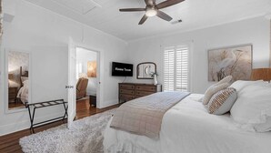Quarto com cama, ventoinha no teto, televisão, cômoda e janela com persianas.