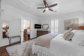 Ein Schlafzimmer mit einem Bett, einem Deckenventilator, einem Fernseher, einer Kommode und einem Fenster mit Jalousien.
