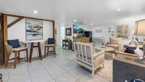 Uma sala espaçosa com mesa de jantar, cadeiras, sofá e cozinha equipada com micro-ondas e frigorífico.