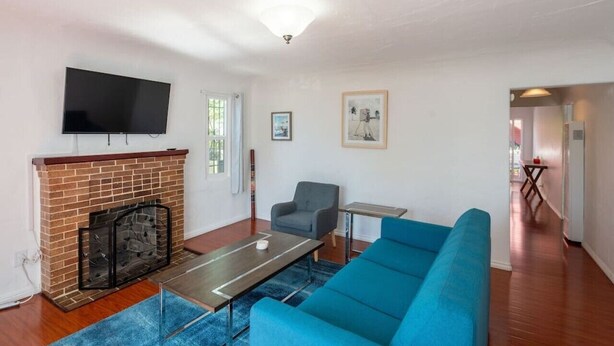 A living room with a brick fireplace, a flat-screen TV, a blue sofa, a coffee table, and a patterned rug. - Bright 3 bedroom Venice House, Short Walk to Beach (Los Angeles)