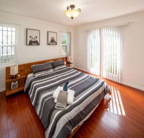 Une chambre à coucher avec un grand lit, un plancher en bois, une table de chevet, une lampe et deux tableaux encadrés au mur.