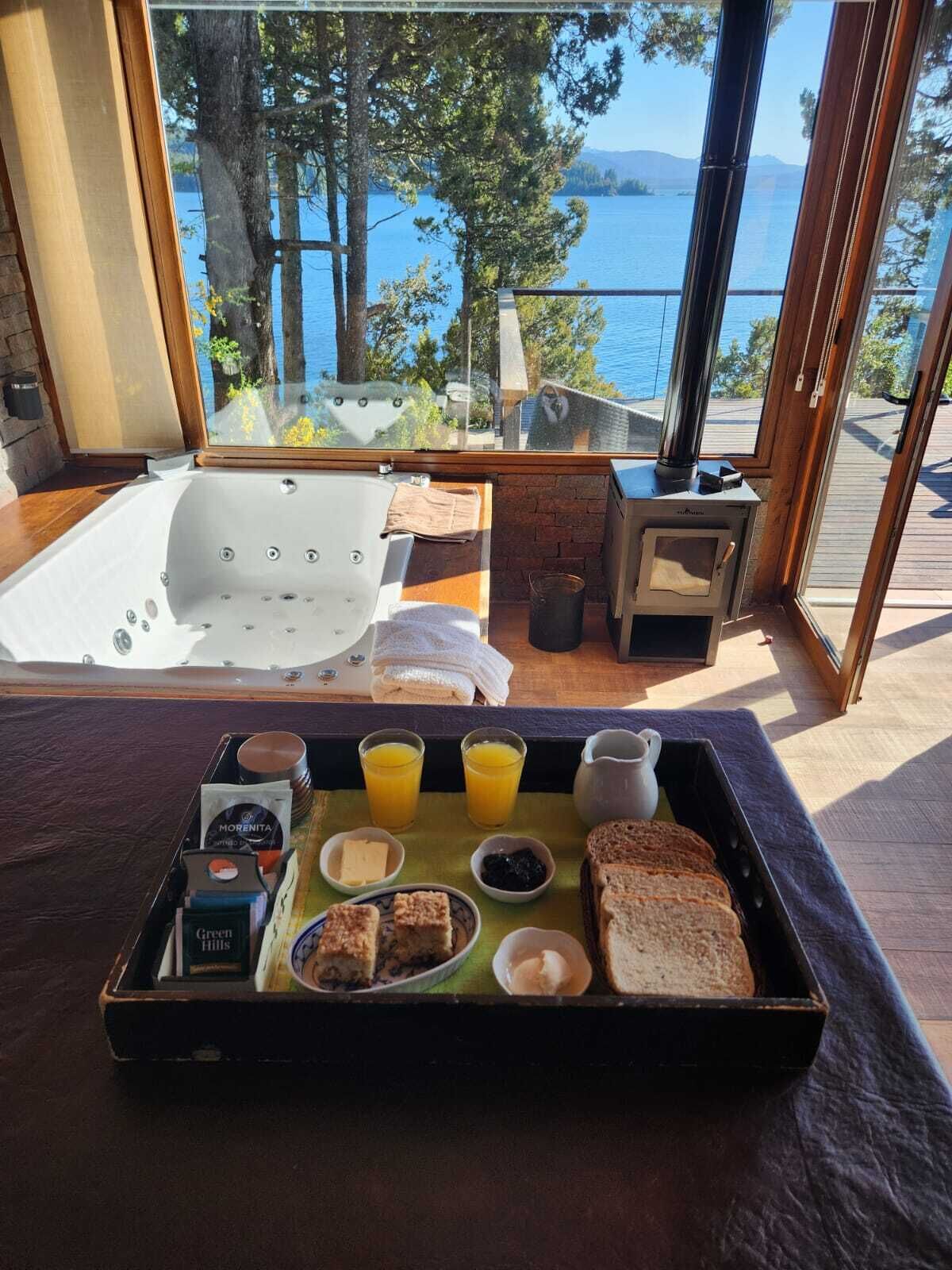 A breakfast tray with toast, butter, jam, and juice, a hot tub, and a wood-burning stove with a view of the lake.