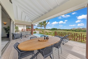 Eine Außenpatio mit Holztisch und -stühlen, einem Pool und Blick auf einen Golfplatz.