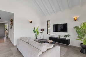 Ein modernes Wohnzimmer mit grauem Sofa, einem schwarzen Couchtisch, einer schwarzen TV-Konsole und einem großen Flachbildfernseher an der Wand.