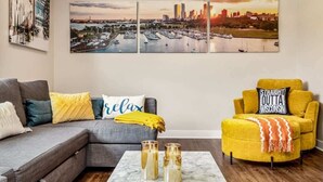 Ein Wohnzimmer mit einer Couch, Sesseln, einem Couchtisch und einem Stadtbild an der Wand.