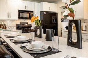 A modern kitchen with white cabinets, a black refrigerator, a microwave, and a dining area set with plates, bowls, and glasses. - Downtown Oasis! Hot Tub, 2 King Beds, Garage Parking, Huge Private Yard! (Milwaukee)