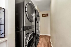 A laundry room with two stacked washers and dryers, a wooden floor, and a sign indicating the room's purpose. - Downtown Oasis! Hot Tub, 2 King Beds, Garage Parking, Huge Private Yard! (Milwaukee)