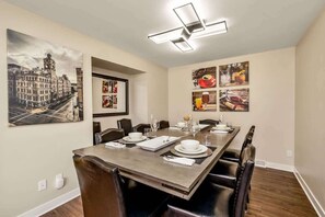 A dining area with a long table set for six, surrounded by chairs. - Downtown Oasis! Hot Tub, 2 King Beds, Garage Parking, Huge Private Yard! (Milwaukee)