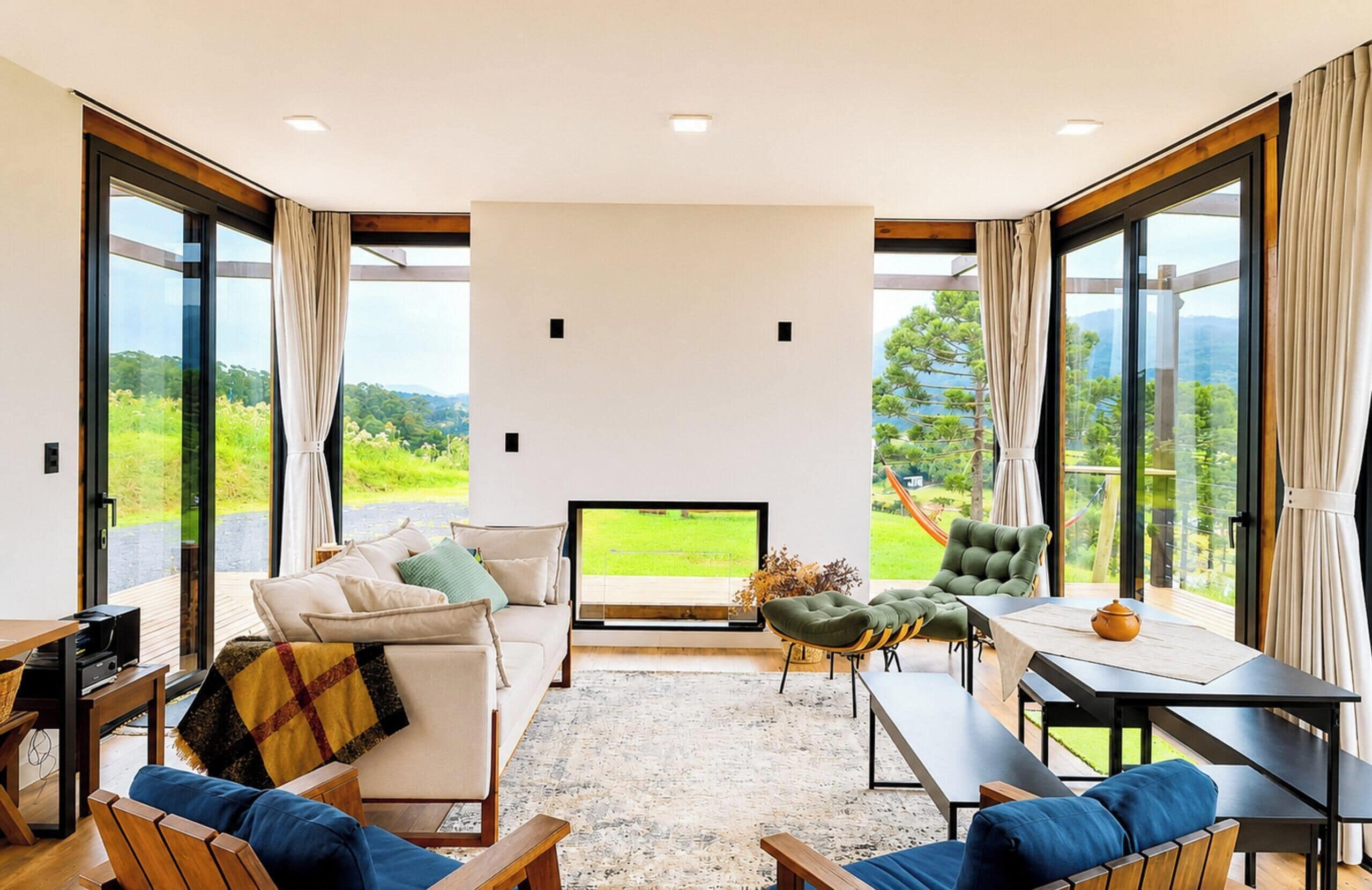A spacious living room with a large flat-screen TV, comfortable seating, and a view of a lush landscape through large windows.