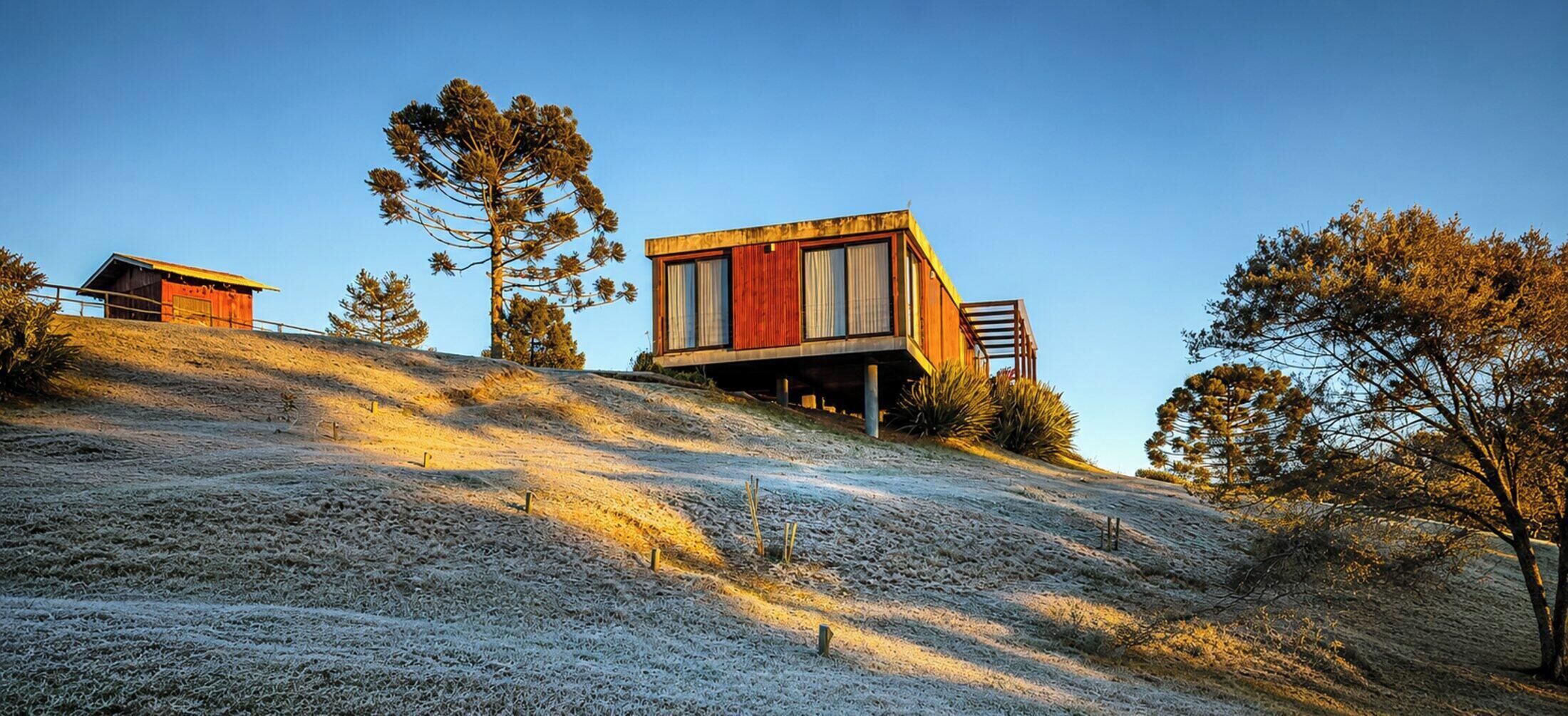 A modern building with a flat roof and large windows, situated on a sloped terrain with sparse vegetation.