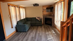 A spacious living area with a sectional sofa, a fireplace, and a wooden staircase. - Bear Hollow 2-bed cabin in charming Old Fort with AC (Old Fort)