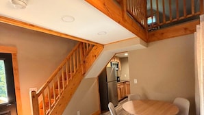A spacious room with a wooden staircase, a dining area with a round table and chairs, and a kitchen in the background. - Bear Hollow 2-bed cabin in charming Old Fort with AC (Old Fort)