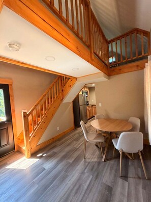 Ein geräumiger Raum mit einer Holztreppe, einem Essbereich mit rundem Tisch und Stühlen sowie einer Küche im Hintergrund.