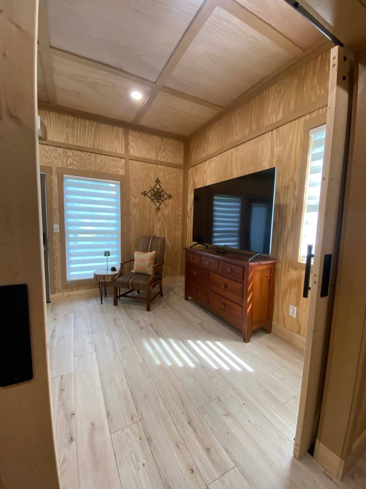 A room with wooden walls and ceiling, a large flat-screen TV, a wooden cabinet, a chair, and a small table.
