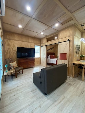 Habitació amb un televisor gran de pantalla plana, un sofà, un llit, un escriptori i un sostre de fusta.