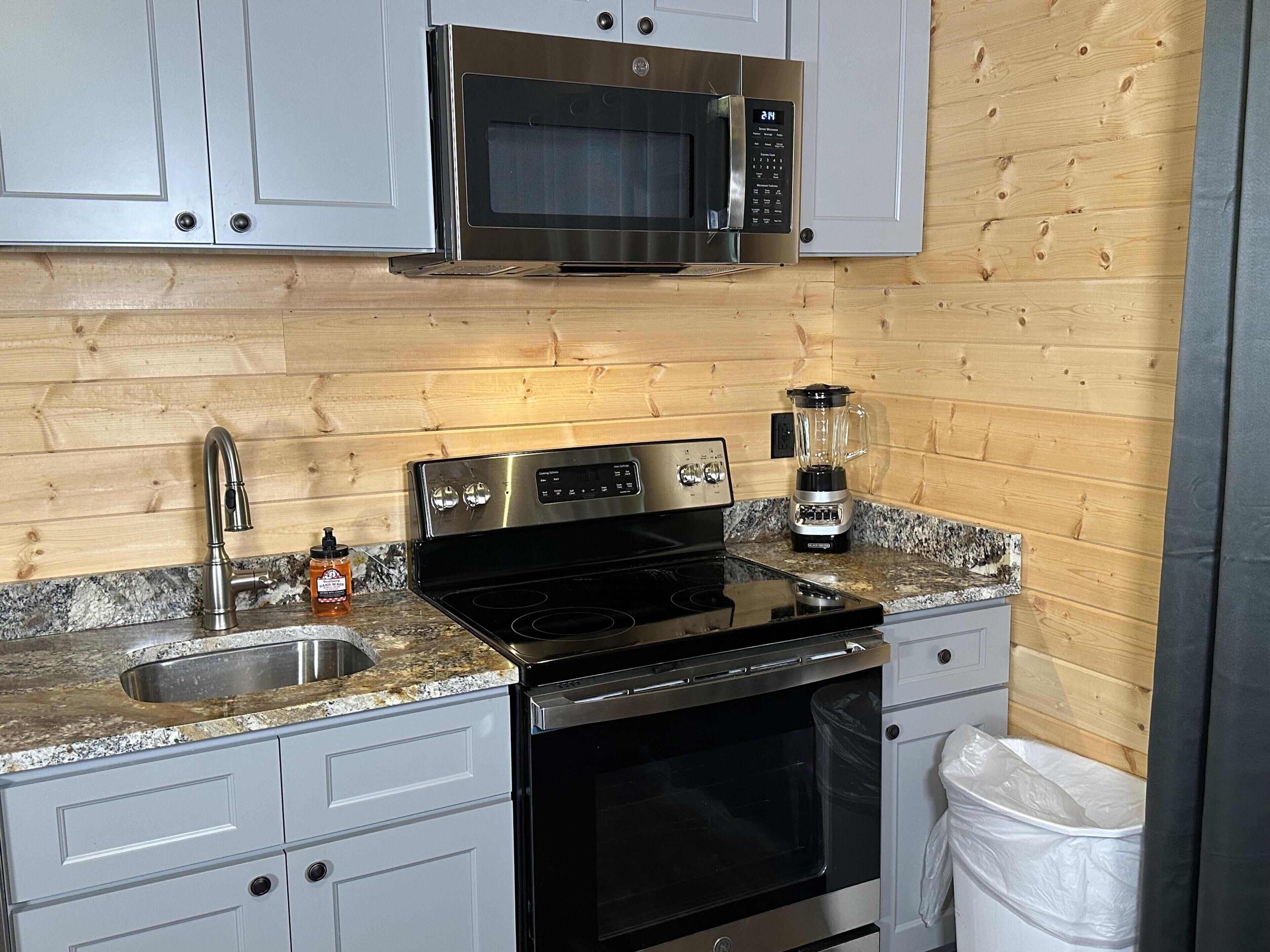A kitchen with a stainless steel microwave, a black stove, a sink, and a blender on the countertop.