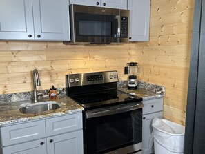 A kitchen with a stainless steel microwave, a black stove, a sink, and a blender on the countertop. - Ward Loft 1 (Fireplace, King Bed, Smart TV) (Canton)