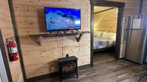A wooden interior with a television on a shelf, a fireplace, a bed, and a refrigerator. - Ward Loft 1 (Fireplace, King Bed, Smart TV) (Canton)