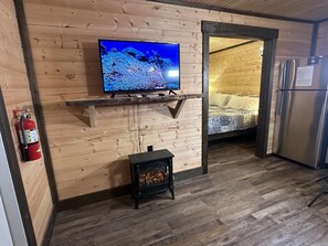 Interior de madeira com televisão numa prateleira, lareira, cama e frigorífico.