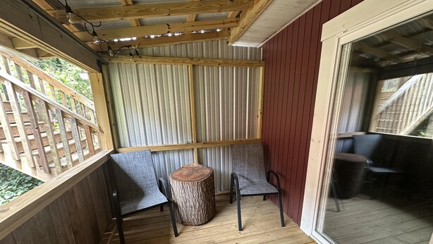 A covered outdoor seating area with a wooden table and two chairs, a metal fence, and a view through a glass door. - Ward Loft 1 (Fireplace, King Bed, Smart TV) (Canton)