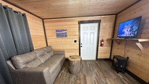 A wooden interior with a sofa, a television, and a fire extinguisher. - Ward Loft 1 (Fireplace, King Bed, Smart TV) (Canton)