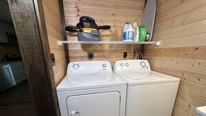 A compact laundry area with two white front-loading washing machines and a shelf above containing cleaning supplies. - Ward Loft 1 (Fireplace, King Bed, Smart TV) (Canton)
