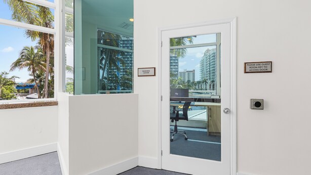 Quarto de hotel com porta de vidro que dá para uma varanda, placa indicando o centro de negócios e porta de acesso ao quarto de hóspedes.