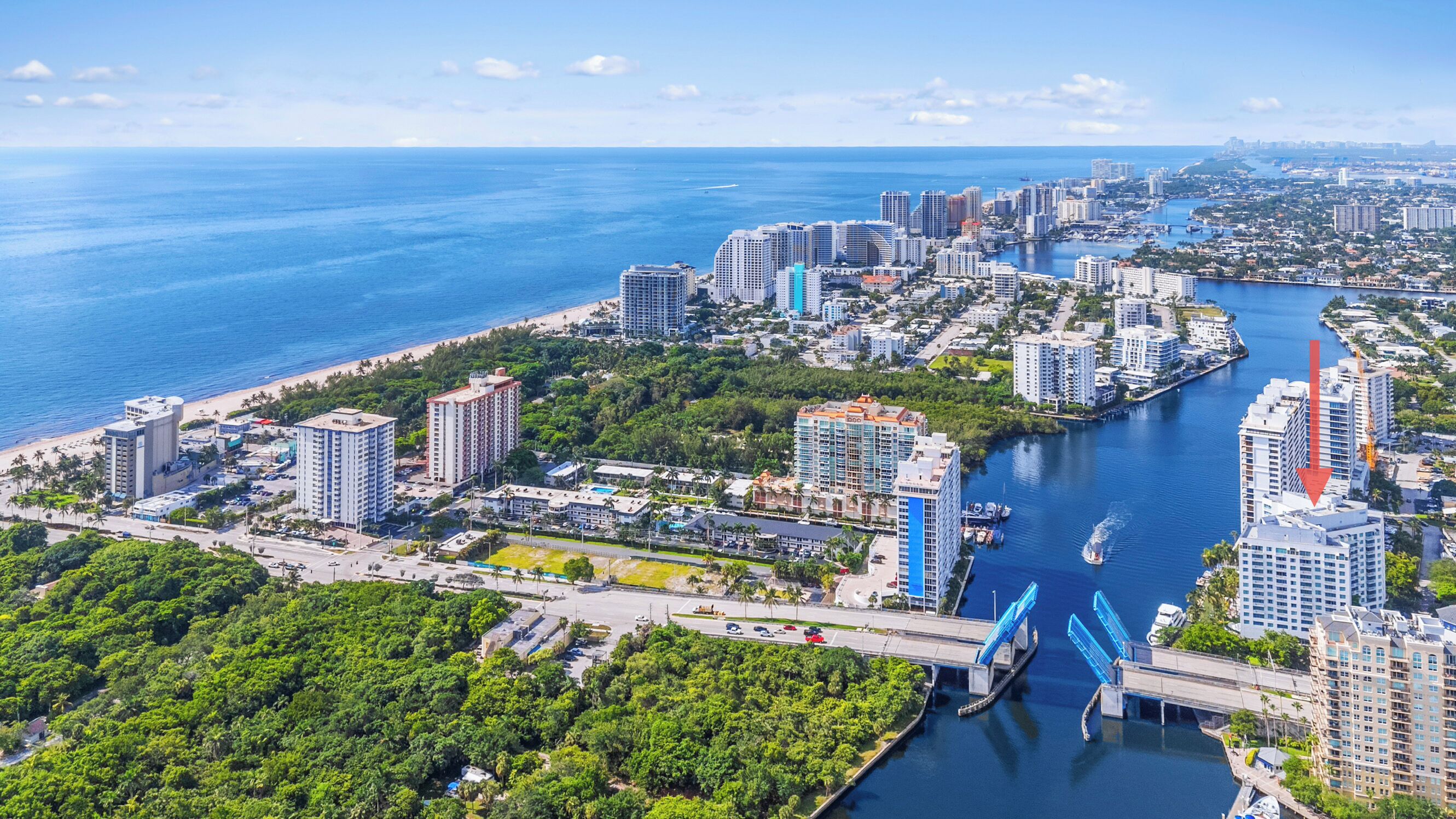 A coastal cityscape with high-rise buildings, a marina, and a bridge.