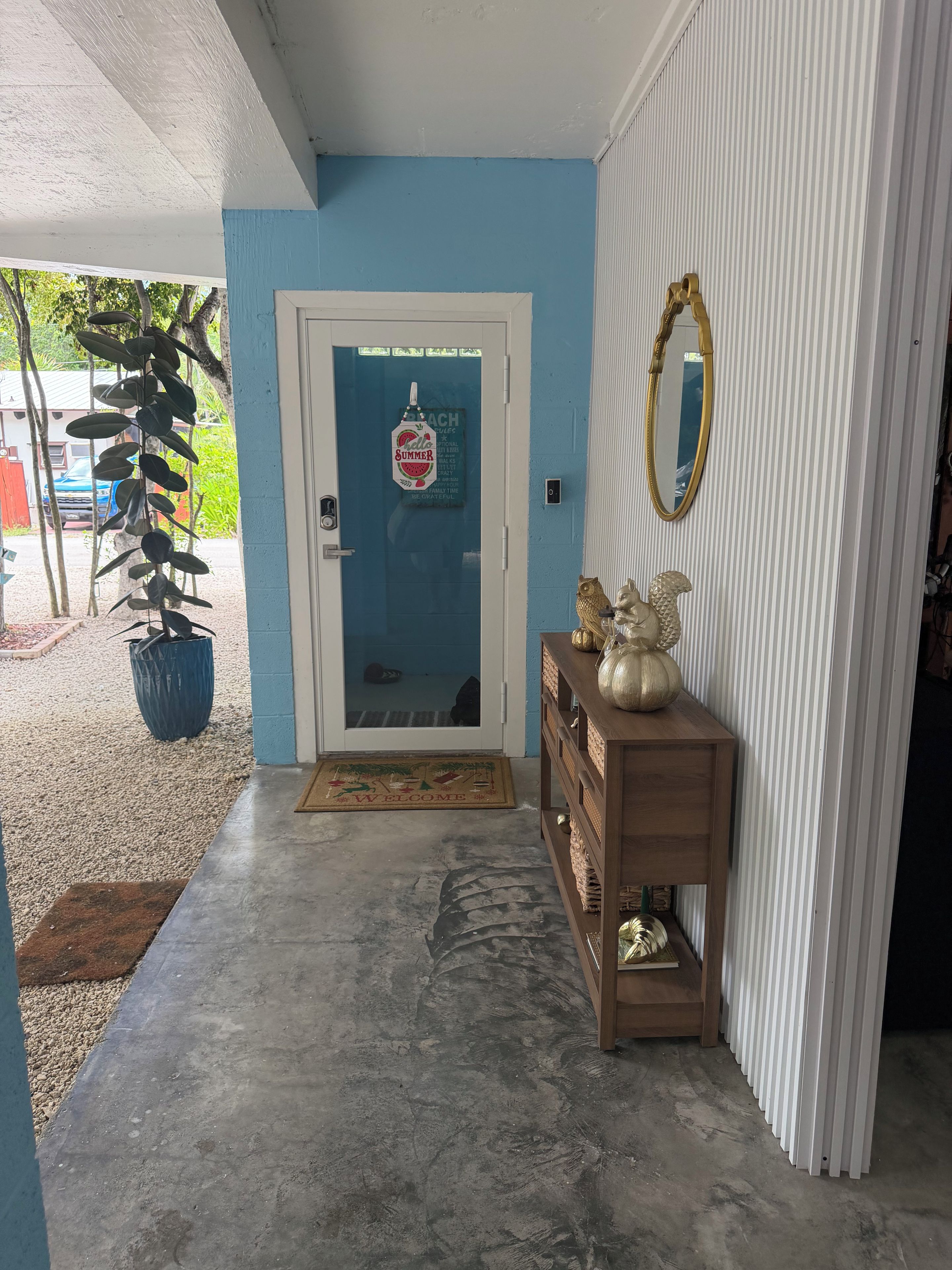 A front entrance with a blue door, a welcome mat, a wooden console table with decorative items, and a potted plant.