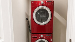 Eine rote, übereinander angeordnete Waschmaschine und ein Trockner in einem schmalen Flur mit Holzboden.