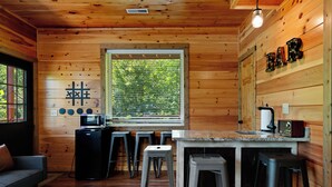 Ein Holzblockhaus-Interieur mit Küchenzeile, Barhocker, einer Bar und einem Fenster mit Blick auf Bäume.