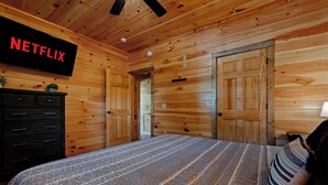 Ein Zimmer mit Holzwänden, einem Bett, einer Kommode und einer Tür.
