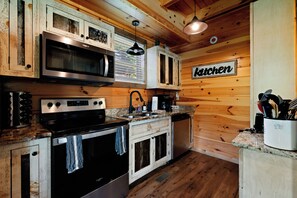 Una cocina con paredes de madera, microondas, estufa, horno y un letrero que dice 'Kitchen'.