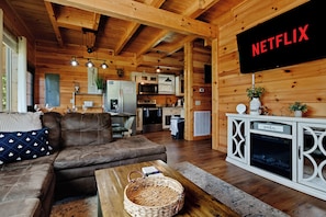 A cozy cabin interior with a living room, kitchen, and a mounted television displaying 'NETFLIX'. - New! Log Cabin w/ Hot Tub, Game Rm, Fire Pit! (Sevierville)