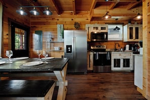 Interior de una cabaña de madera con cocina, una mesa de comedor para dos personas y un refrigerador.
