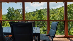 Ein überdachter Außenbereich mit Tisch und Stühlen, mit Blick auf einen bewaldeten Hang.