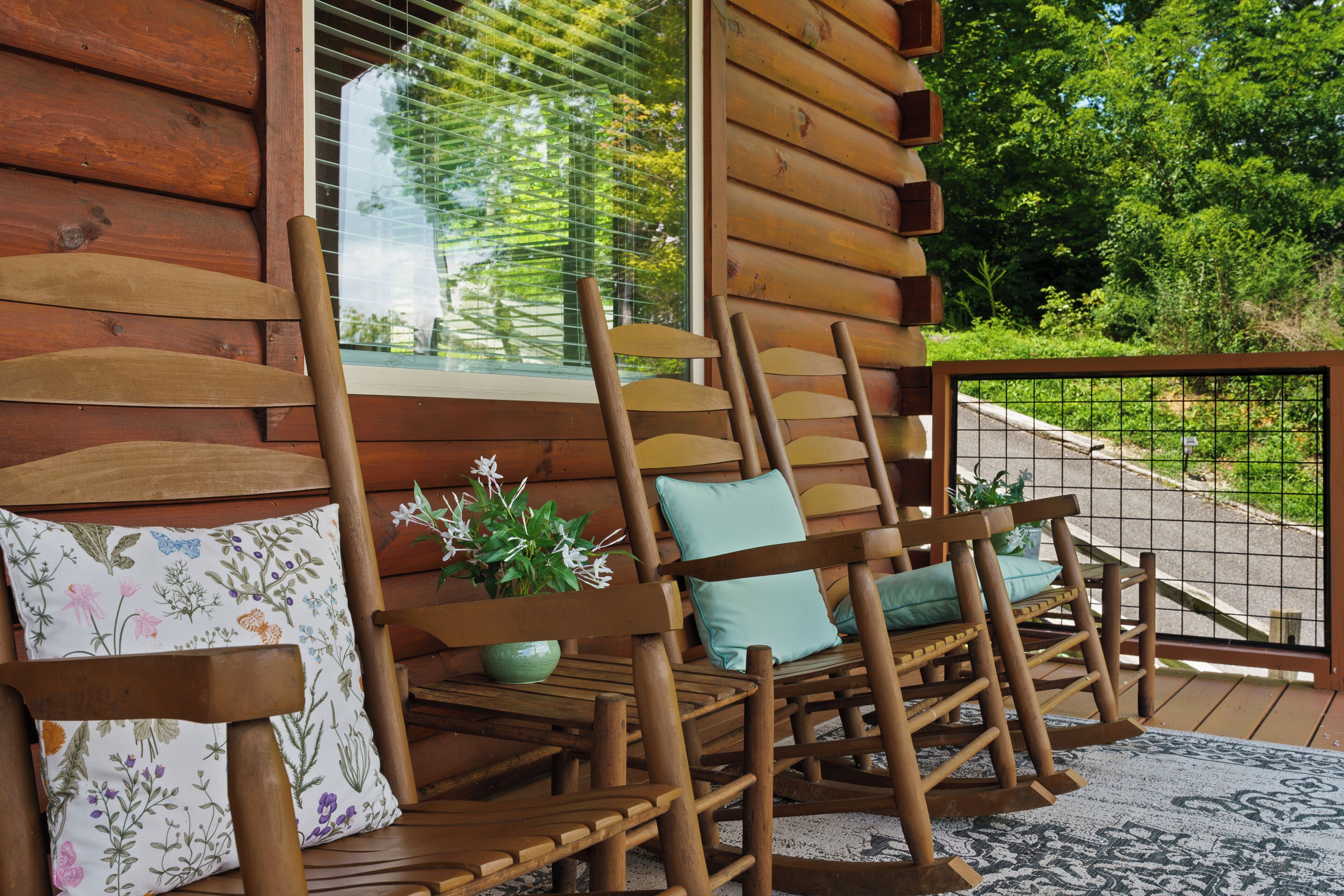 A wooden deck with two rocking chairs, each with a cushion and a small potted plant.