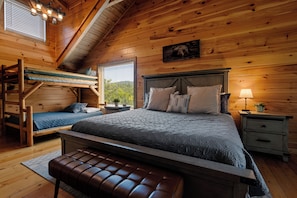 Ein Schlafzimmer einer Holzhütte mit einem Etagenbett, einem großen Bett mit vielen Kissen, einer Bank, einem Nachttisch und einer Lampe.
