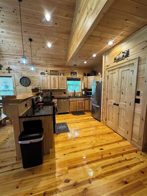 A wooden cabin interior with a kitchen, wooden cabinets, a refrigerator, and a window with a view. - Hound Dog Heaven a peaceful mountain retreat (Almond)