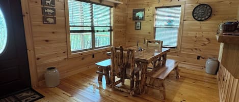 L’intérieur d’un chalet en bois comprend une table à manger, des bancs, un luminaire suspendu et un plafond en bois.