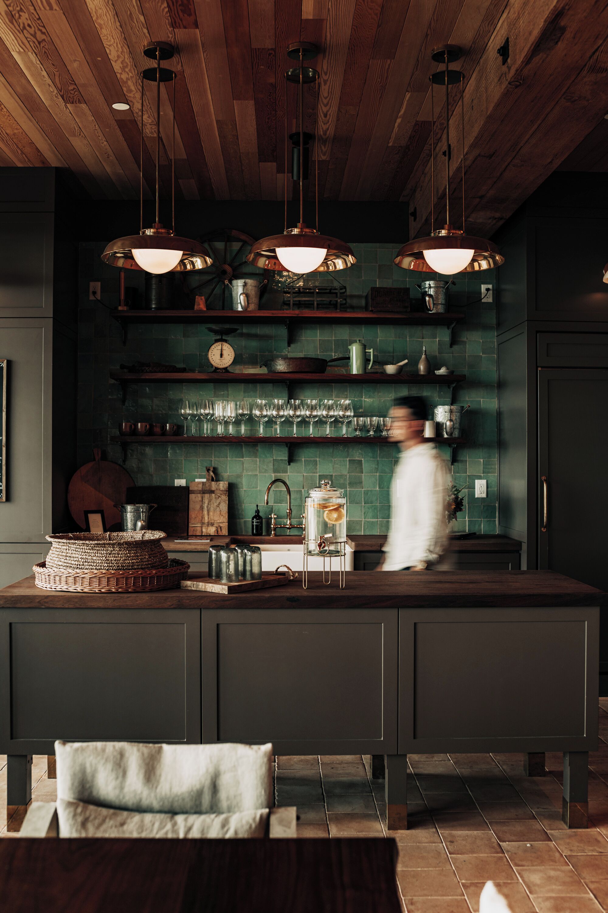 Une cuisine avec un plafond en bois, un pare-feu vert et des luminaires suspendus.