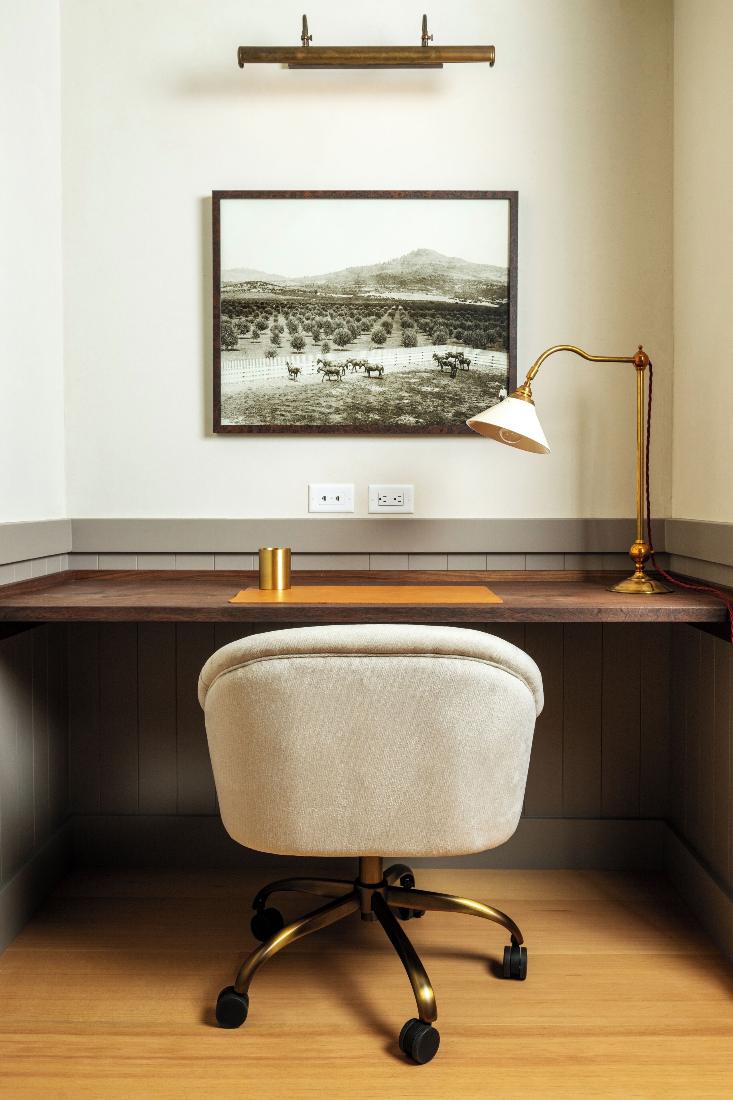En arbetsplats med ett skrivbord, en stol, en lampa och ett inramat fotografi på väggen.