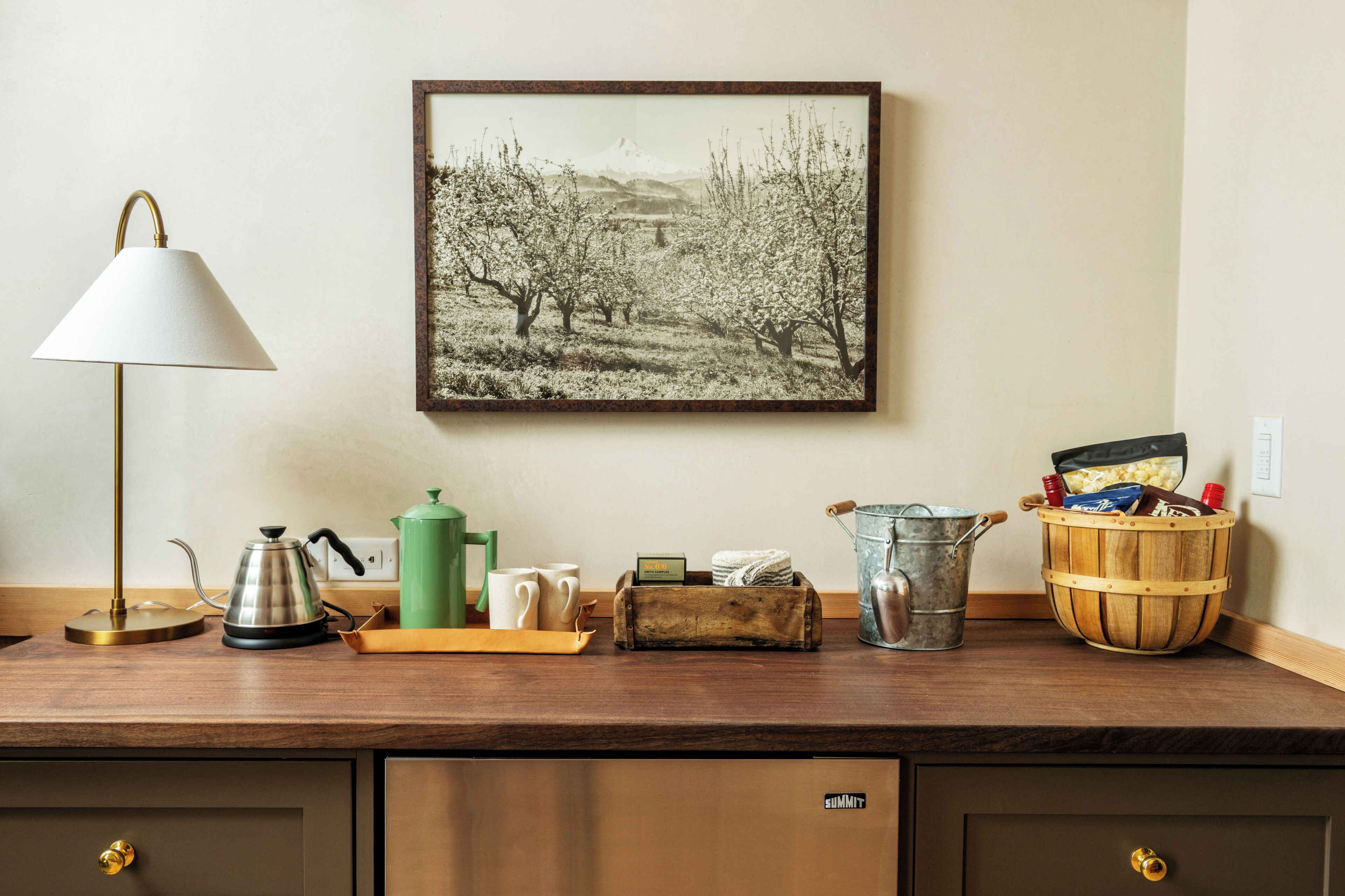 A kitchen counter with a coffee maker, kettle, mug, and a wooden basket containing various items.