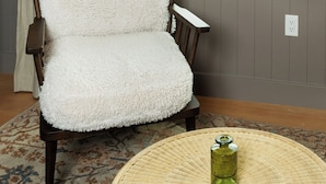Una silla con asiento y respaldo blancos y mullidos, ubicada frente a una ventana con vista a un paisaje verde.