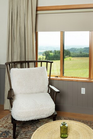 Una silla con asiento y respaldo blancos y mullidos, ubicada frente a una ventana con vista a un paisaje verde.
