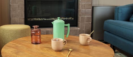 A round wooden table with a coffee pot, two cups, and a spoon.