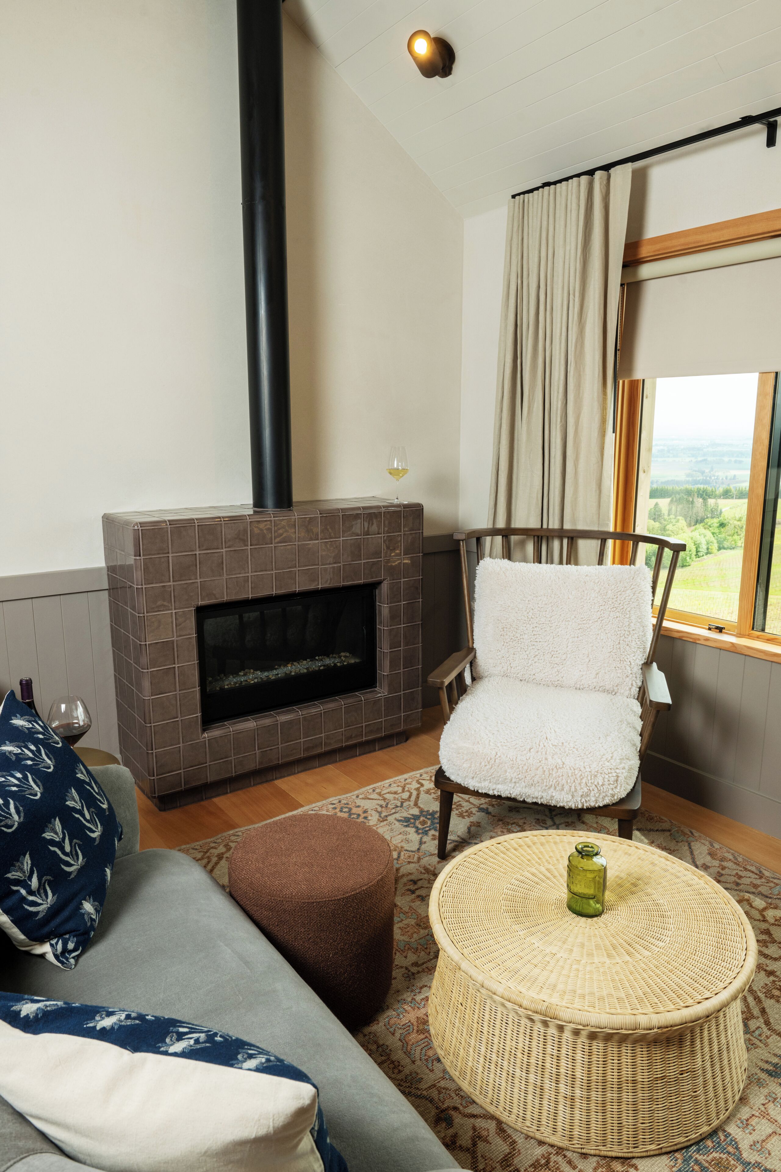 A living room with a fireplace, a sofa, a chair, a round coffee table, and a view through a window.